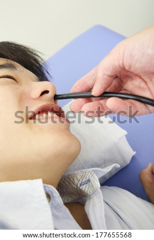 Hand of a Japanese doctor inserting endoscope through the patient\'s nose
