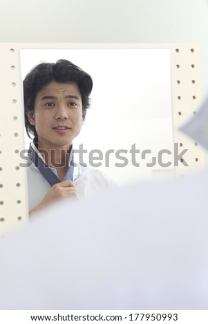 Japanese man tying a tie while looking in the mirror
