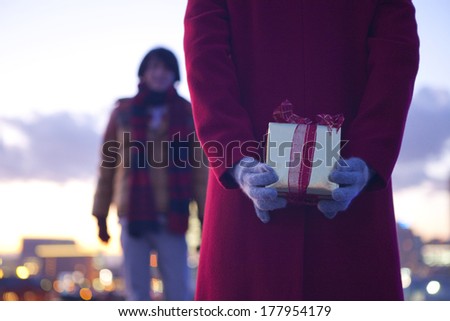 Back of a Japanese woman trying to pass a Christmas gift to man