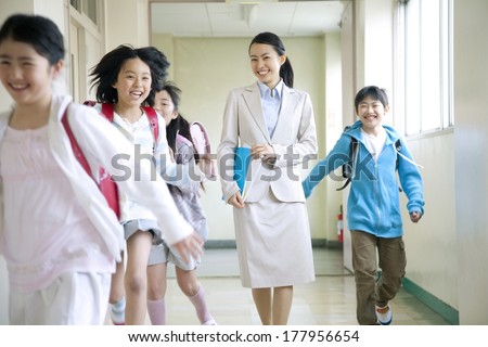 Primary Japanese boy and Japanese girl who are playing with a female teacher walking the corridor