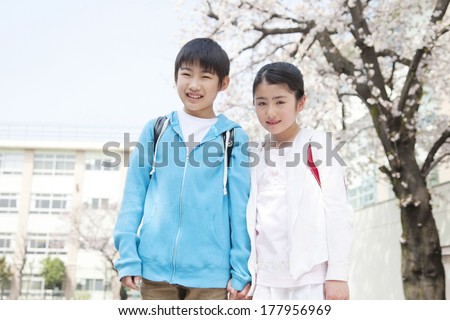 Primary Japanese boy and Japanese girl who are standing under the cherry tree