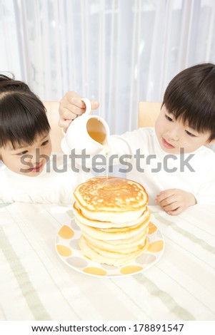 Japanese Girl and boy pouring honey over pancakes