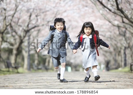 Primary Japanese boy and Japanese girl who are running along the path lined with cherry blossom trees