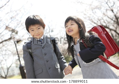Primary Japanese boy and Japanese girl who walks on the path lined with cherry blossom trees
