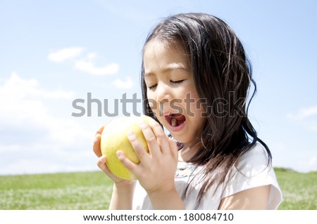 Japanese girl about to eat a large, green apple in a meadow