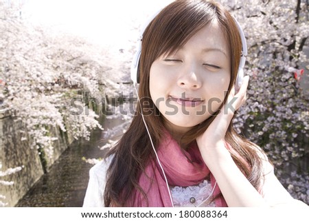 Japanese woman listening to music in the background of cherry tree