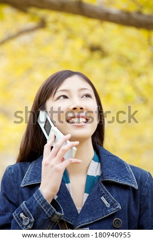 Japanese woman speaking on mobile phone while walking on the street lined with the ginkgo tree