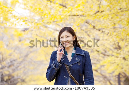 Japanese woman speaking on mobile phone while walking on the street lined with the ginkgo tree