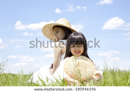 Young girls and Japanese woman sitting back to back in the grassland
