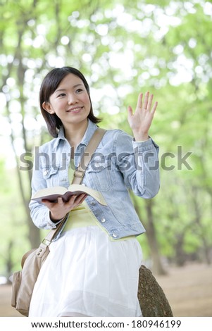 A Japanese student waving while holding on to a dictionary,