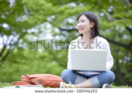 Japanese Student working on their laptops while laying on grass,