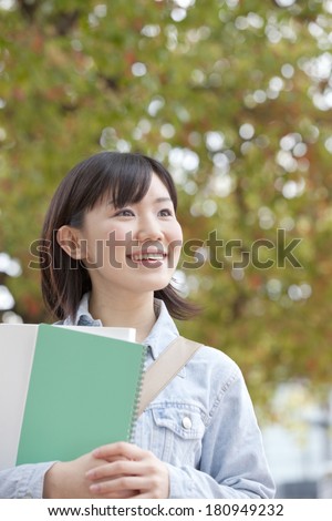 A Japanese student holding onto a notebook, smiling,