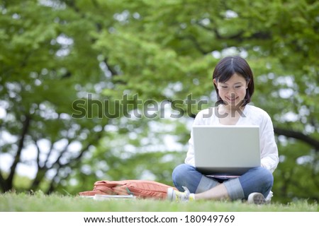 Japanese student working on her laptop while laying on grass,
