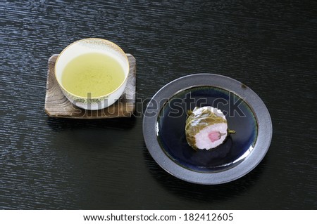 Tea and bean paste rice cake wrapped in a cherry leaf and put on a table