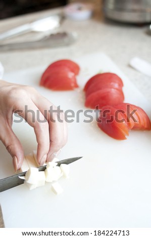 Woman\'s hand cubing cheese on a cutting board