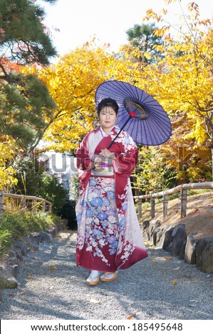 Middle-aged woman walking along garden pathway dressed in Japanese traditional outfit