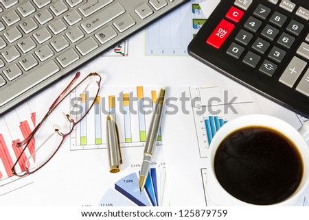 Desk of a businessman . Computer, business graphs, calculator, glasses,pen and coffee.