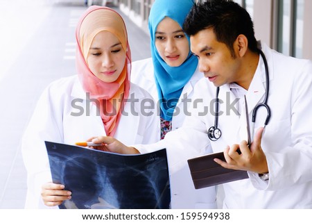 Experienced male doctor guide two female junior doctors examining a file in in front of hospital