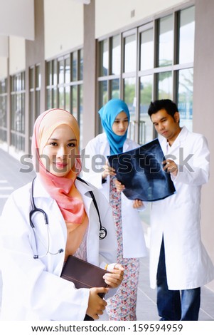 Close up of young beautiful doctor with two junior doctor discussing at the background