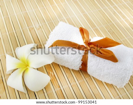 rolled up white spa towel with flower on bamboo mat background