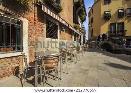 Wooden tables on narrow street among typical colorful houses and small bridge in Venice, Italy.
