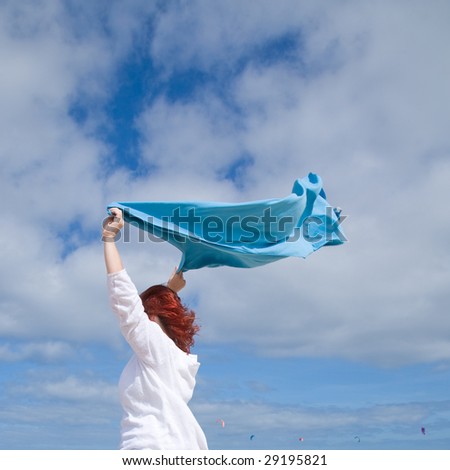 woman with bright red hair holding a blue towel, blown by the wind