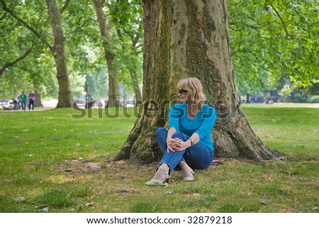 attractive middle-age woman sitting under a huge plane tree in Hyde park, London
