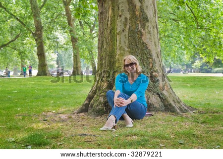 attractive middle-age woman sitting under a huge plane tree in Hyde park, London