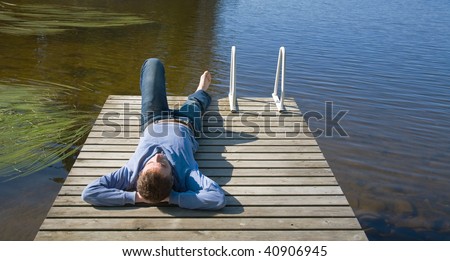 Northern summer - middle age man laying on an old wooden pier, suntanning, shallow lake, morning sun