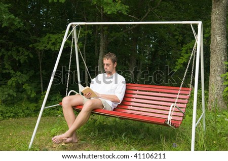 middle aged caucasian man reading a bok siting on old swing bench - old summer house situation