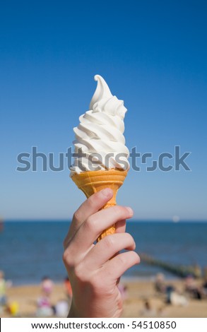 large portion of soft ice-cream in child\'s hand; beach, sea and blue sky in the background;