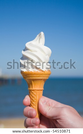 large portion of soft ice-cream in man's hand; sea and blue sky in the background