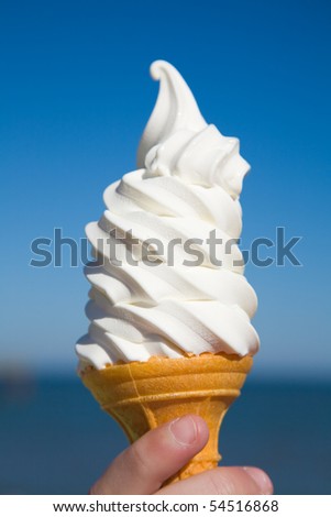 large portion of soft ice-cream in child\'s hand, sea and blue sky in the background