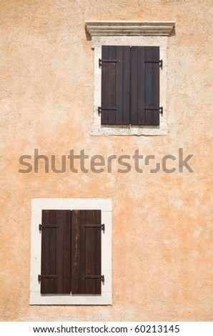 two  asymmetrical windows with dark wooden closed shutters in light terracotta-colored wall