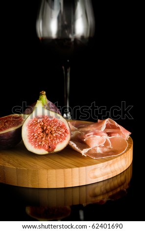 fresh figs; Prosciutto and red wine on small round chopping board; on black reflective surface