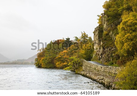 driving in Lake District, Cumbria, UK - narrow road along Ullswater lake shore under steep rock face