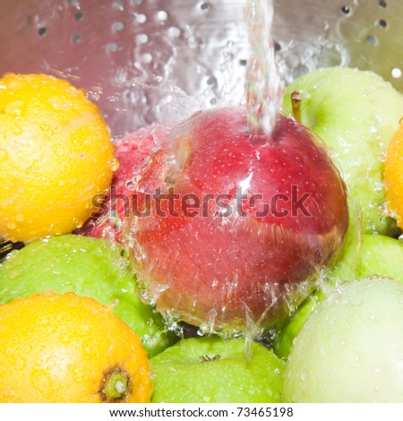 red and green apples and lemons being washed in stainless steel colander under tap