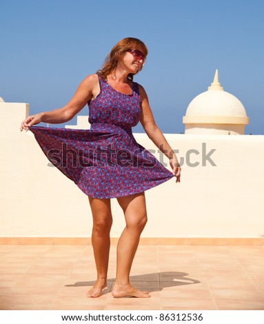 age doesn't matter - tanned, fit middle-aged woman dances on the subroof in short flared dress