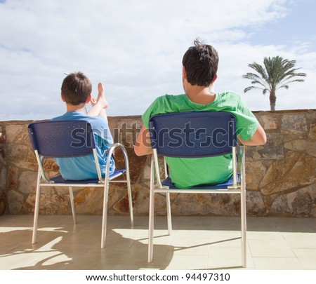 lazy afternoon - two caucasian boys sittings on sunlit patio, with their feet on a low wall,