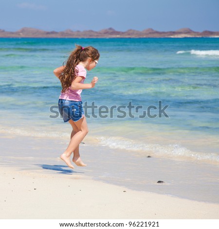 little girl with long brown hair in ponytail in pink t-shirt and denim shorts by the ocean