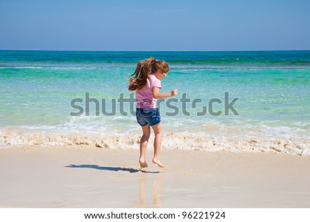 little girl with long brown hair in ponytail in pink t-shirt and denim shorts by the ocean
