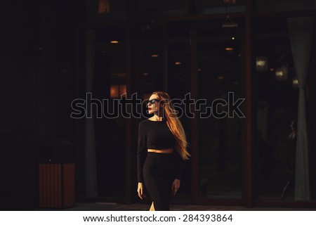 Beautiful  young woman wearing sunglasses, black top and pencil skirt, walks on the street. Fashion photo
