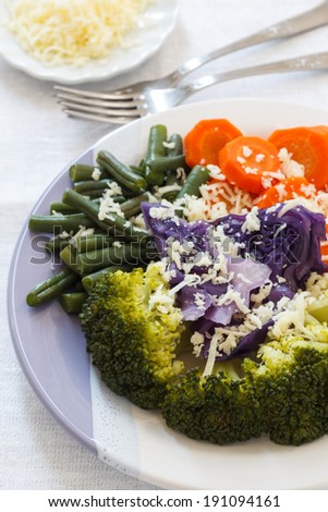 Steamed broccoli carrots, green beans, purple cabbage on plate with cheese. Selective focus