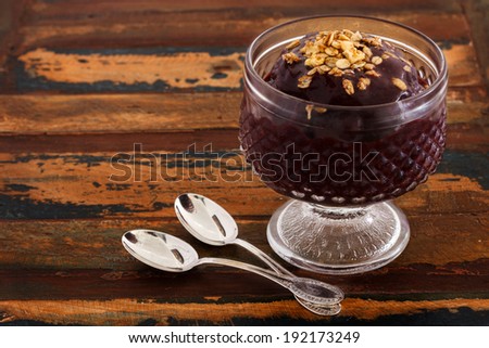 Acai pulp juice in glass with muesli  spoon on wooden table. Selective focus on muesli