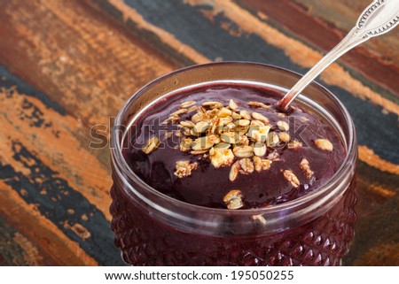 Acai pulp juice in glass with muesli  spoon on wooden table close. Selective focus on muesli