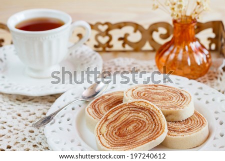 Bolo de rolo (swiss roll, roll cake) typical Brazilian dessert cup of tea vase on tray. Selective focus
