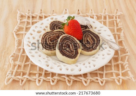 Bolo de rolo (swiss roll, roll cake) Brazilian chocolate dessert with strawberry on white plate wicker wooden table. Selective focus