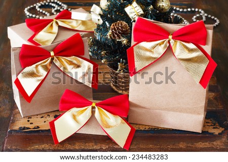 Gifts paper package with red golden bow near small Christmas tree. Selective focus on bow.
