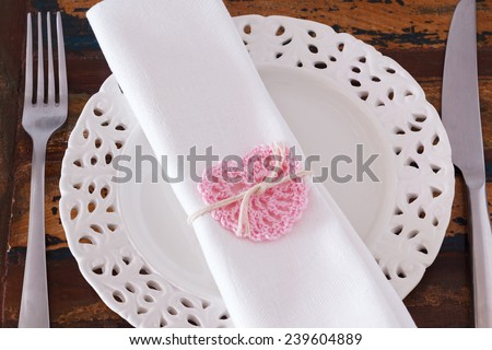 Decoration for Saint Valentine\'s day: White plate serviette with handmade pink crochet heart. Selective focus