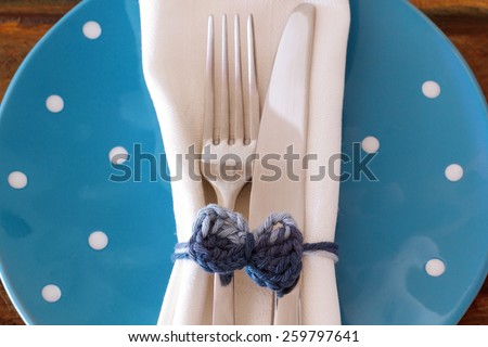 Table decoration: White plate serviette fork knife with handmade crochet bowl on blue plate. Selective focus
